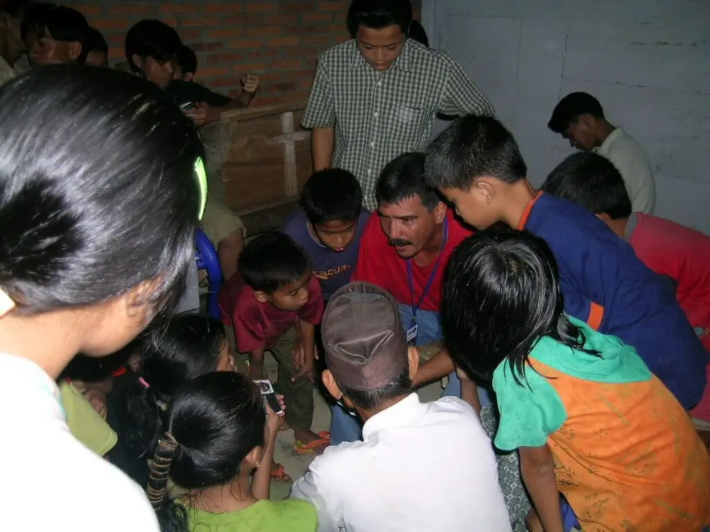 Man teaching with young children crowded around him