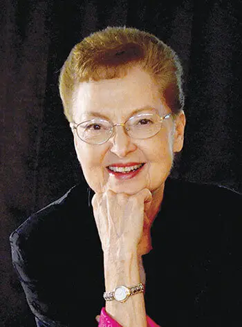 Author Rosalie Hall Hunt smiling at camera with hand under chin and black background