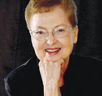 Author Rosalie Hall Hunt smiling at camera with hand under chin and black background